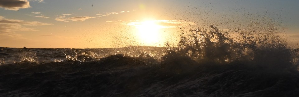 Ocean wave breaking in front of sunset